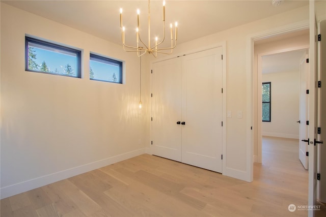 unfurnished bedroom featuring a notable chandelier, light hardwood / wood-style floors, and a closet