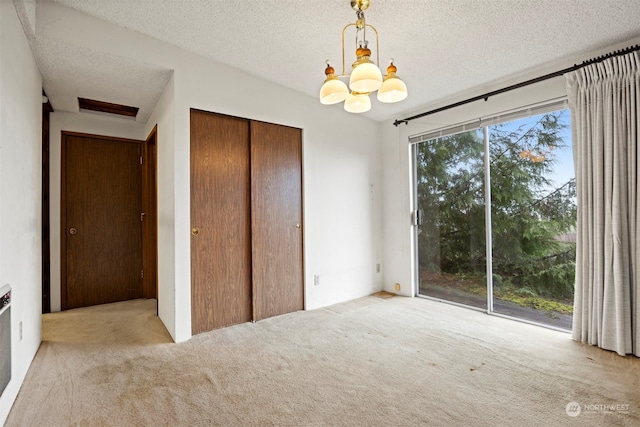 interior space with a closet, light colored carpet, a textured ceiling, and a chandelier