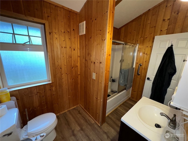 full bathroom featuring wood walls, hardwood / wood-style floors, bath / shower combo with glass door, and vaulted ceiling