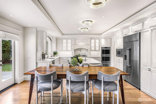 kitchen with a raised ceiling, sink, built in appliances, light hardwood / wood-style floors, and white cabinetry