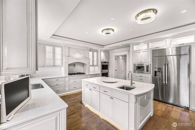 kitchen with white cabinets, built in appliances, a kitchen island with sink, and sink