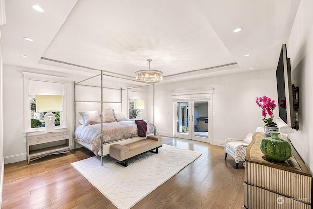 bedroom featuring access to outside, a raised ceiling, an inviting chandelier, and hardwood / wood-style flooring