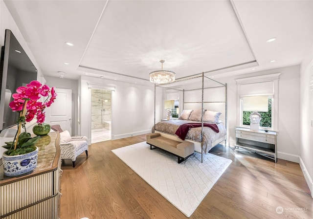 bedroom featuring wood-type flooring, ensuite bath, a raised ceiling, and a notable chandelier