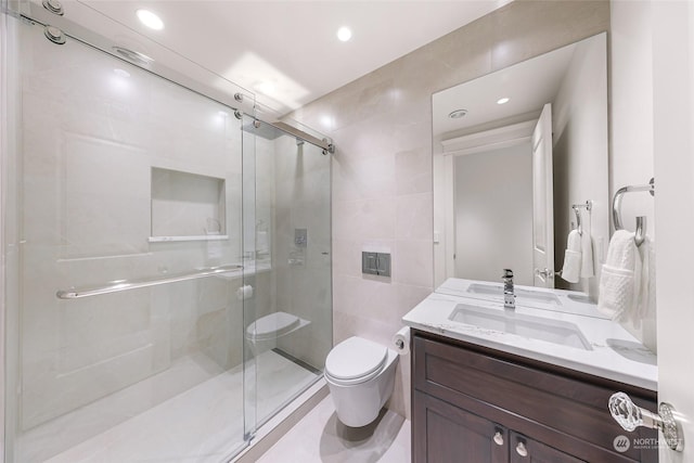 bathroom with a shower with door, vanity, tile walls, and toilet