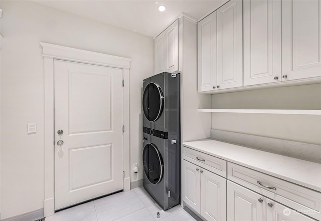 clothes washing area featuring cabinets, stacked washer / dryer, and light tile patterned flooring