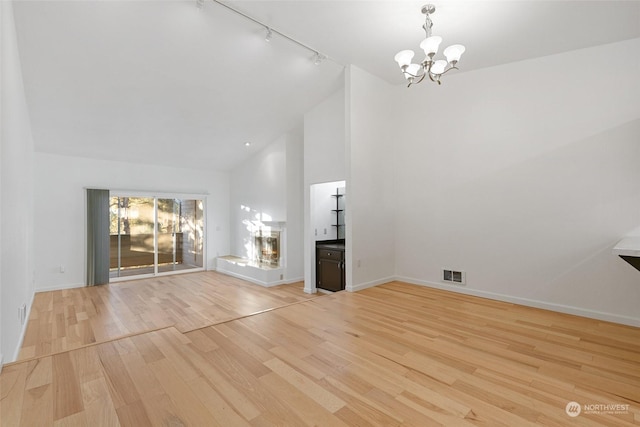 unfurnished living room with light wood-type flooring, track lighting, high vaulted ceiling, and a notable chandelier