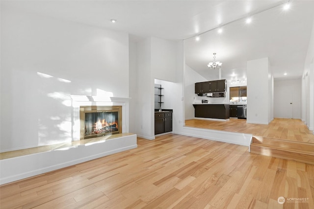 unfurnished living room with light hardwood / wood-style flooring, rail lighting, a high ceiling, and an inviting chandelier