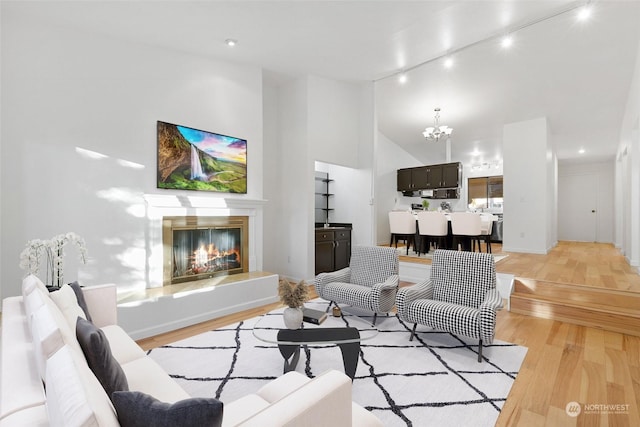 living room featuring light hardwood / wood-style flooring, high vaulted ceiling, a notable chandelier, and rail lighting