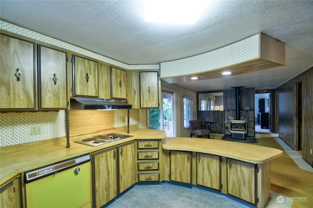 kitchen with a wood stove, a textured ceiling, appliances with stainless steel finishes, light colored carpet, and kitchen peninsula