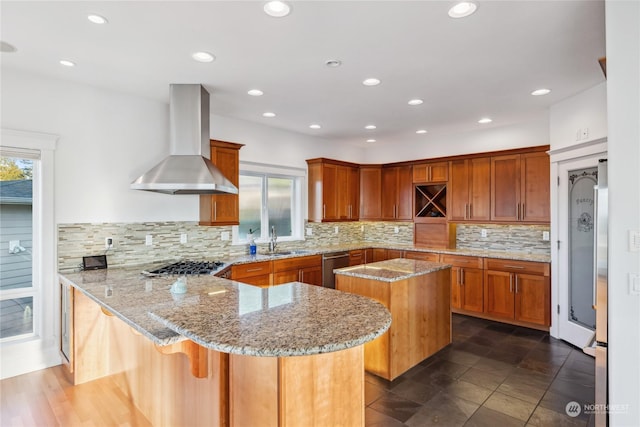 kitchen featuring kitchen peninsula, light stone counters, wall chimney exhaust hood, a kitchen island, and a breakfast bar area