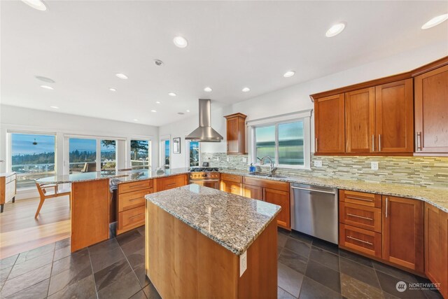 kitchen featuring a center island, wall chimney exhaust hood, stainless steel appliances, sink, and light stone counters