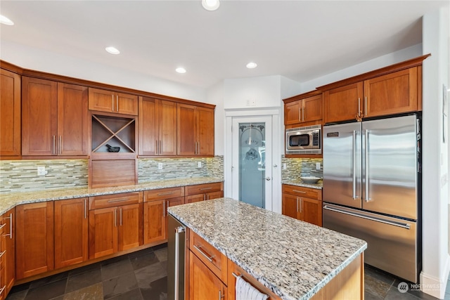 kitchen with decorative backsplash, a kitchen island, light stone counters, and appliances with stainless steel finishes