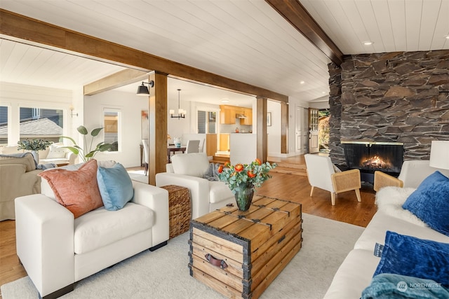 living room featuring vaulted ceiling with beams, light hardwood / wood-style flooring, a stone fireplace, and wood ceiling