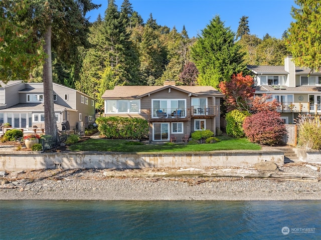 view of front of property with a water view, a balcony, and a front lawn