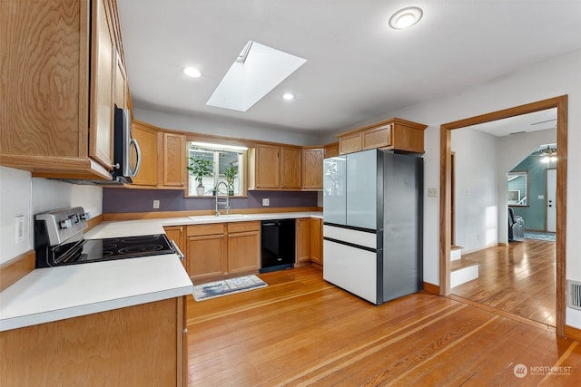 kitchen featuring sink, a skylight, ceiling fan, light wood-type flooring, and appliances with stainless steel finishes