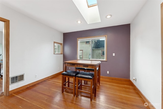 dining room with hardwood / wood-style floors and a skylight