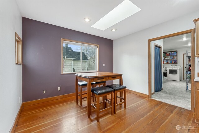 dining room featuring a skylight, washer and clothes dryer, and light hardwood / wood-style floors