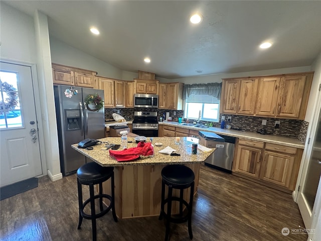 kitchen with a center island, dark hardwood / wood-style floors, vaulted ceiling, a breakfast bar area, and appliances with stainless steel finishes