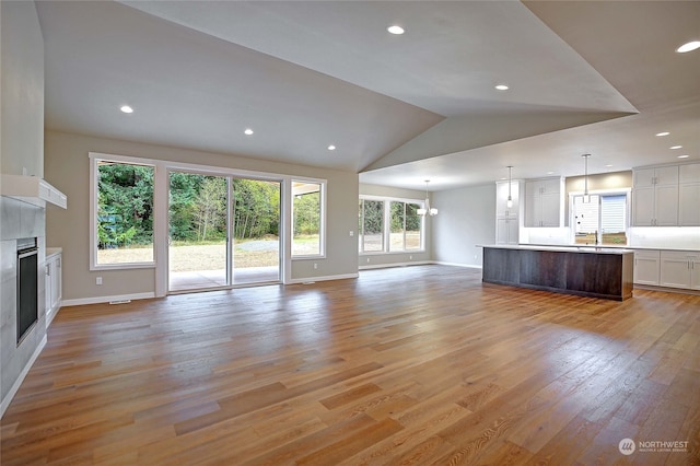 unfurnished living room featuring a healthy amount of sunlight, vaulted ceiling, sink, and light hardwood / wood-style flooring