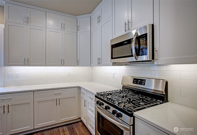 kitchen with backsplash, stainless steel appliances, white cabinetry, and dark wood-type flooring