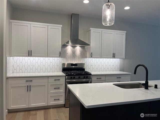 kitchen featuring light stone countertops, stainless steel gas range, sink, wall chimney range hood, and decorative light fixtures