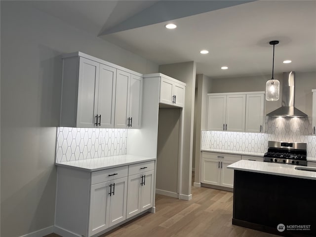 kitchen featuring white cabinetry, hanging light fixtures, wall chimney range hood, and stainless steel range with gas stovetop