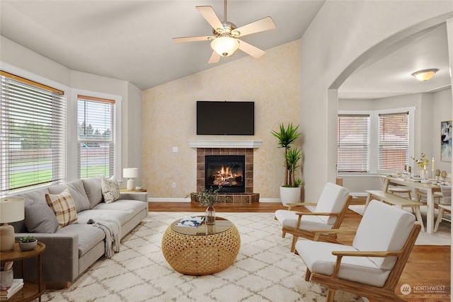 living room featuring ceiling fan, lofted ceiling, a fireplace, and light wood-type flooring