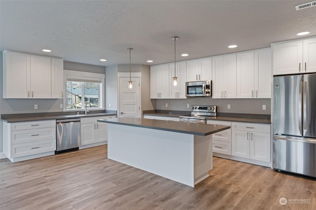 kitchen featuring appliances with stainless steel finishes, pendant lighting, white cabinetry, a center island, and light hardwood / wood-style flooring