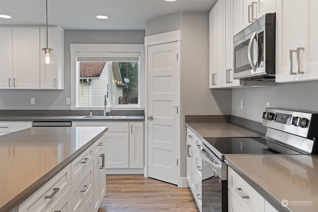 kitchen featuring appliances with stainless steel finishes, sink, white cabinets, hanging light fixtures, and light wood-type flooring