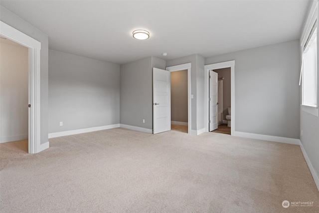 unfurnished bedroom featuring light carpet and ensuite bath