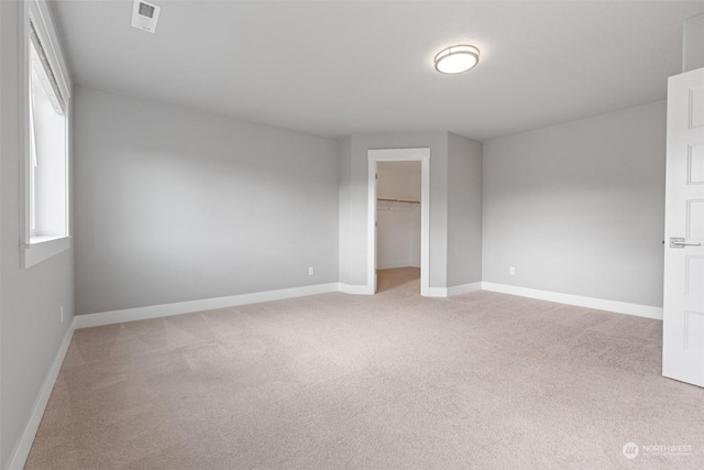 unfurnished bedroom featuring a walk in closet, light carpet, and a closet