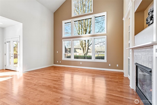 unfurnished living room with high vaulted ceiling, light wood finished floors, a tile fireplace, and baseboards