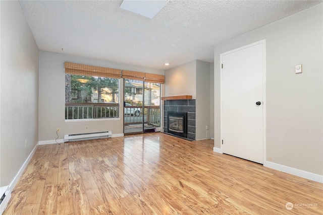 unfurnished living room featuring a tiled fireplace, light hardwood / wood-style flooring, a baseboard radiator, and a textured ceiling