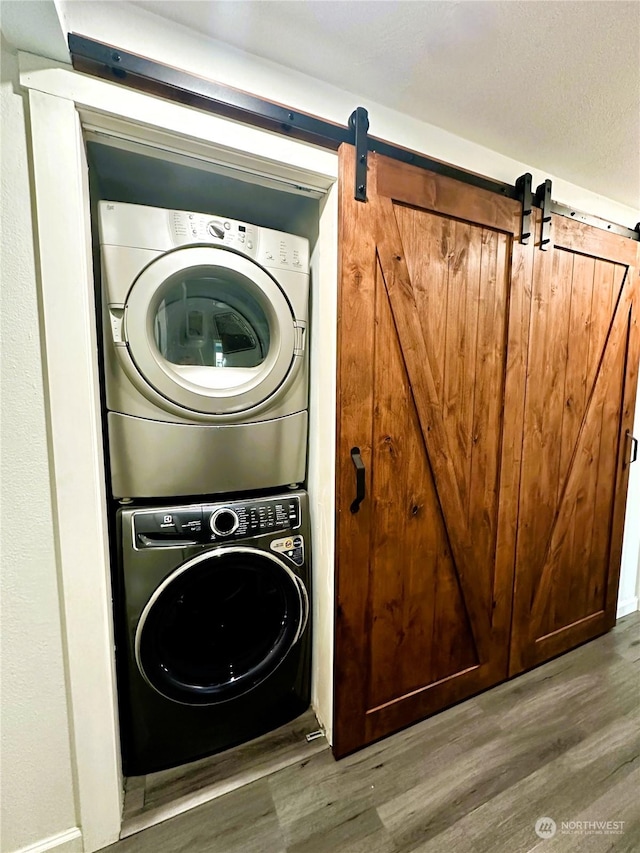 laundry area featuring hardwood / wood-style floors, a barn door, and stacked washing maching and dryer