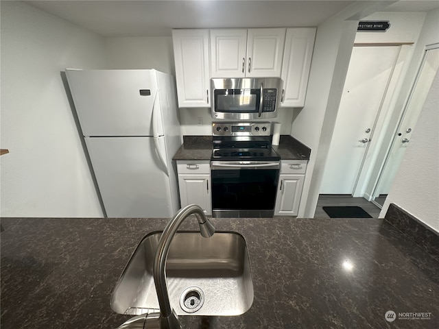 kitchen with appliances with stainless steel finishes, white cabinetry, dark stone counters, and sink