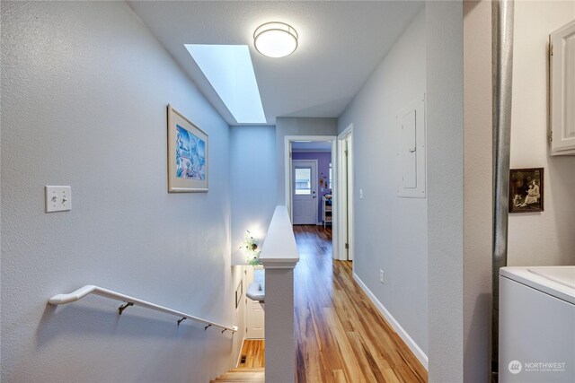 hall with washer / dryer, electric panel, light hardwood / wood-style floors, and a skylight