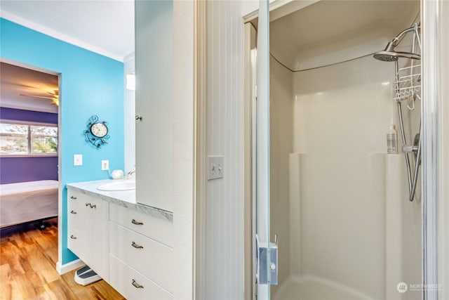 bathroom featuring vanity, hardwood / wood-style flooring, ceiling fan, ornamental molding, and walk in shower