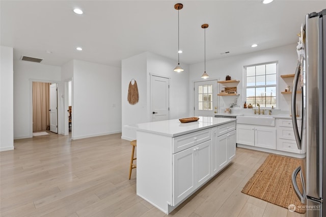 kitchen with a center island, white cabinets, hanging light fixtures, light hardwood / wood-style flooring, and stainless steel fridge