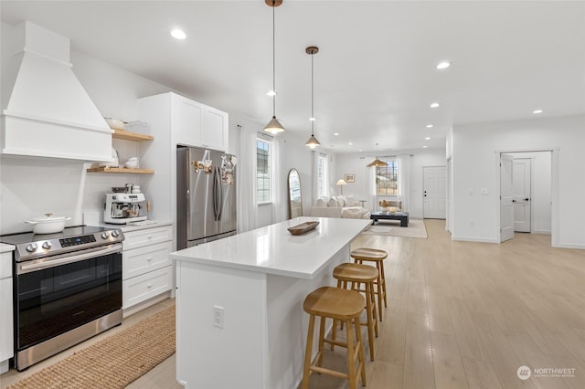 kitchen with white cabinets, hanging light fixtures, light hardwood / wood-style flooring, custom range hood, and stainless steel appliances