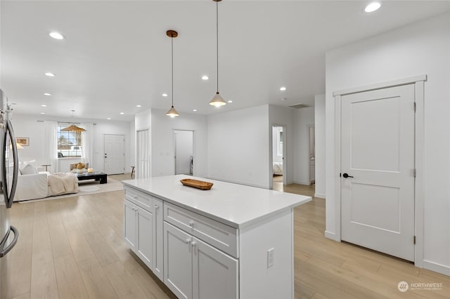 kitchen featuring white cabinets, light wood-type flooring, a center island, and hanging light fixtures