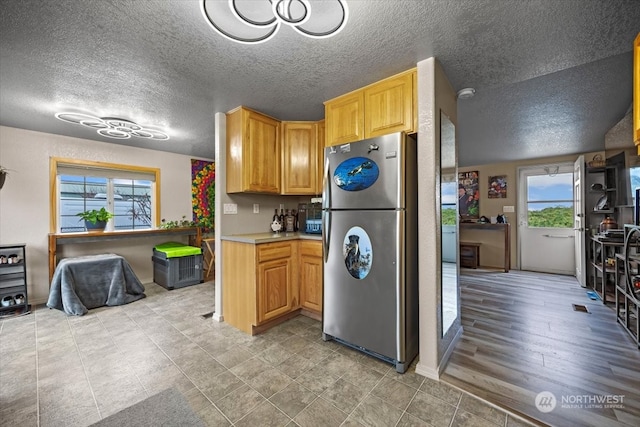 kitchen featuring stainless steel fridge, light wood-type flooring, and a textured ceiling