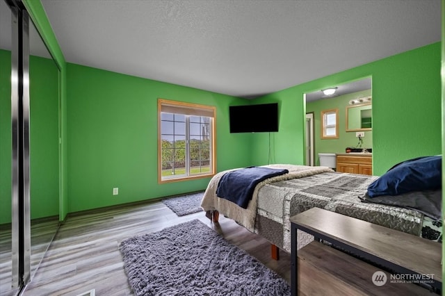 bedroom with ensuite bathroom, a textured ceiling, and light wood-type flooring