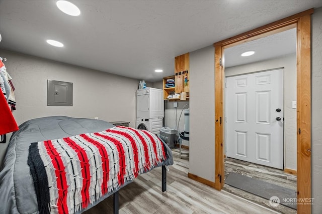 bedroom with light hardwood / wood-style floors, stacked washer and dryer, and electric panel