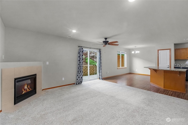 unfurnished living room with ceiling fan with notable chandelier, a tiled fireplace, and light colored carpet