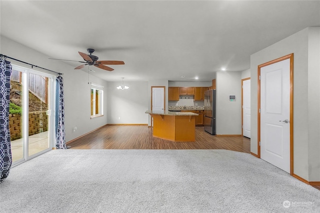 kitchen with light colored carpet, a center island, ceiling fan with notable chandelier, and stainless steel refrigerator