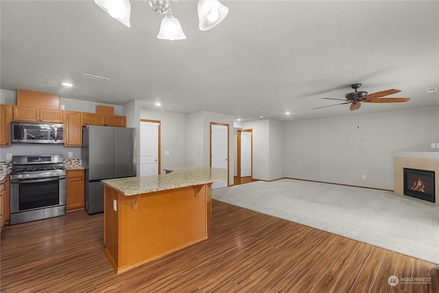 kitchen featuring appliances with stainless steel finishes, hanging light fixtures, dark hardwood / wood-style flooring, a kitchen bar, and a kitchen island