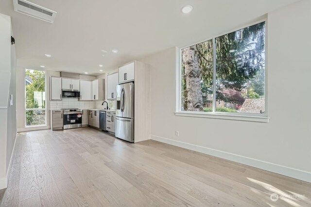 kitchen with white cabinets, sink, light wood-type flooring, appliances with stainless steel finishes, and tasteful backsplash