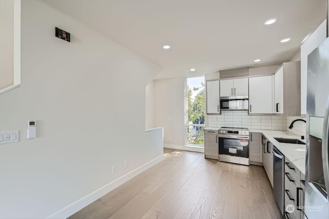 kitchen with sink, light wood-type flooring, appliances with stainless steel finishes, light stone counters, and white cabinetry