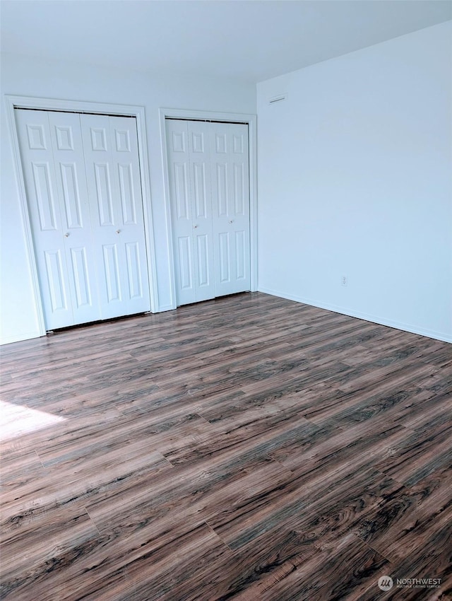 unfurnished bedroom featuring dark wood-type flooring and two closets