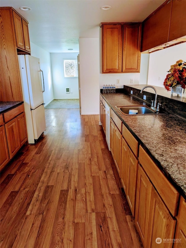 kitchen featuring white appliances, dark stone counters, brown cabinetry, dark wood-style floors, and a sink